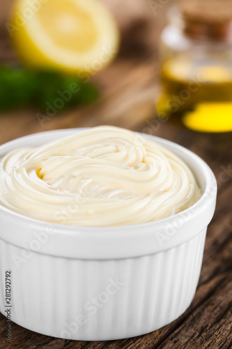 Mayonnaise sauce in white bowl with parsley, lemon and oil in the back (Selective Focus, Focus in the middle of the mayonnaise)