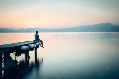Rear view of man sitting on jetty and looking at view photo