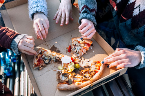 Four friends eating pizza outdoors, partial view