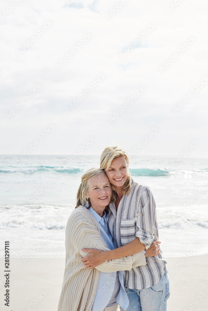 Senior woman and her adult daughter standing on the beach, embracing Senior woman and her adult daughter standing on the beach, embracing