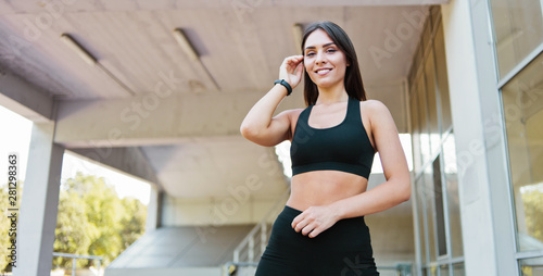 Portrait of smiling young woman in sportswear posing outdoors in urban environment