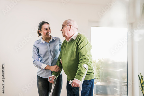 Young woman supporting senior man walking on crutches photo