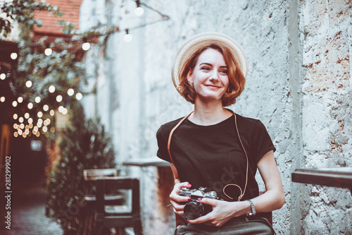 Young hipster female journalist with retro camera  sits on a chair and smiles outdoors against the backdrop of garlands photo