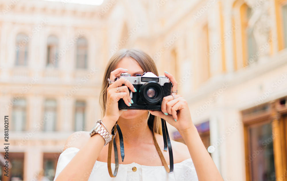 Young attractive photographer woman with retro camera in her hands while taking pictures at urban old architecture. Discover new places