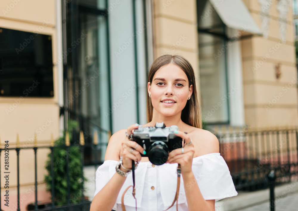 Cheerful blond woman holding retro camera in the urban environment