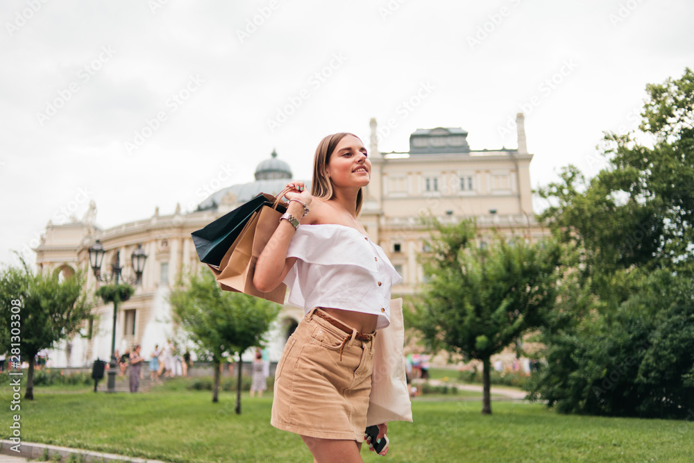 Cheerful beautiful shopaholic woman with paper shopping bags posing at camera outdoors