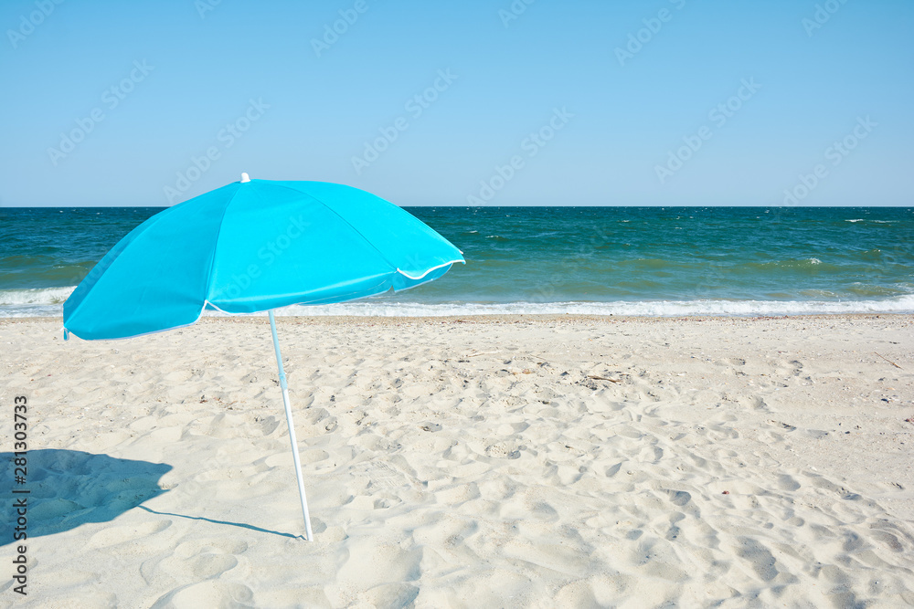 Turquoise beach umbrella by sea shore. Sunny hot day on the sandy beach.