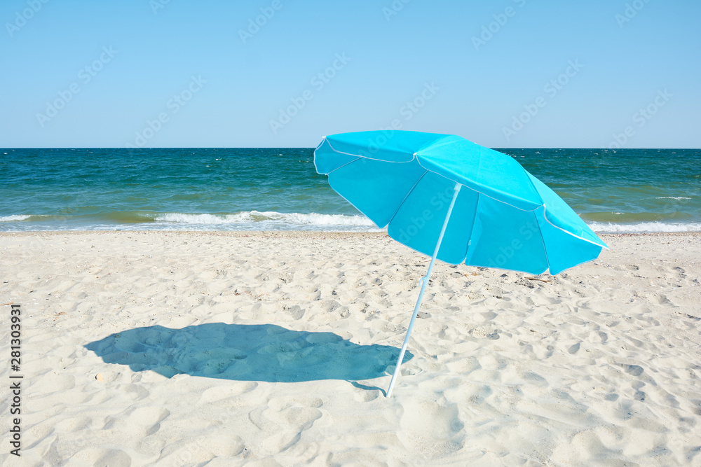 Turquoise beach umbrella by sea shore. Sunny hot day on the sandy beach.