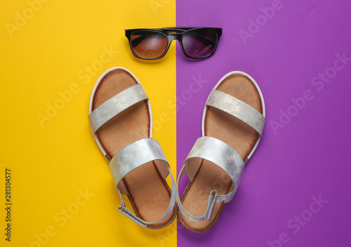 Creative summer beach flat lay. Leather women's sandals, sunglasses on purple yellow background. Top view