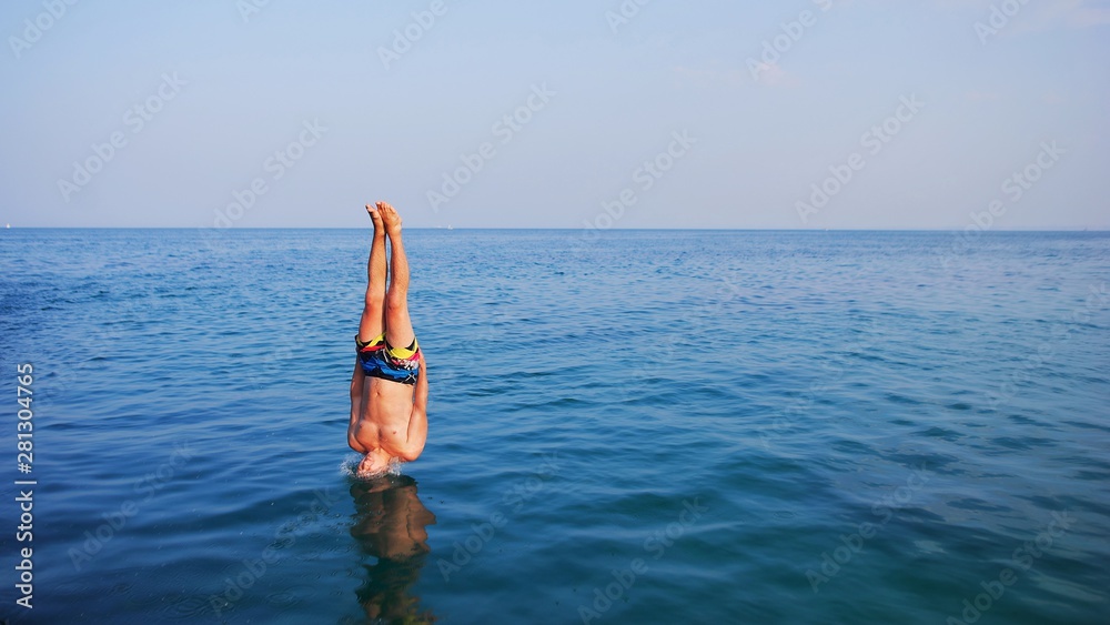 Young man jumping off cliff into blue water ocean at sunset. Active outdoor, holiday adventure, tourism action, healthy summer joy, Fun activity lifestyle. Crazy adult guy in swimwear fly from climb. Young man jumping off cliff into blue water ocean at sunset. Active outdoor, holiday adventure, tourism action, healthy summer joy, Fun activity lifestyle. Crazy adult guy in swimwear fly from climb.