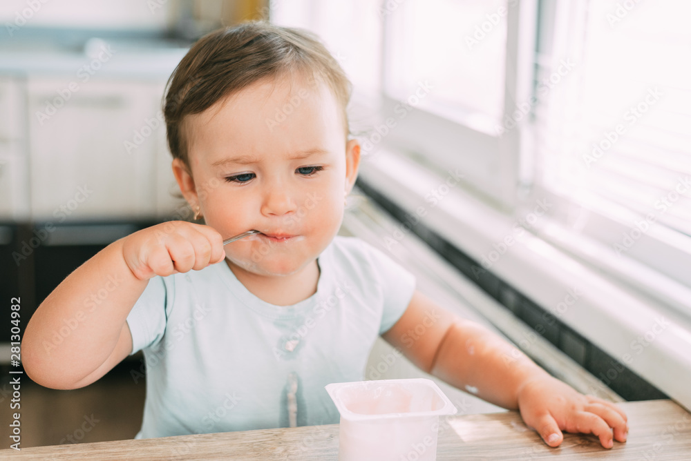 Little girl in the afternoon in the kitchen eating yogurt Little girl in the afternoon in the kitchen eating yogurt