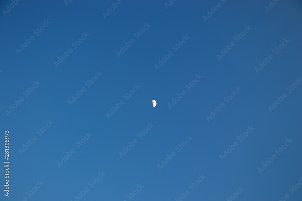 Half of the moon on a clear blue sky in the afternoon. A small satellite of the earth ra monophonic background. Half of the moon on a clear blue sky in the afternoon. A small satellite of the earth ra monophonic background.