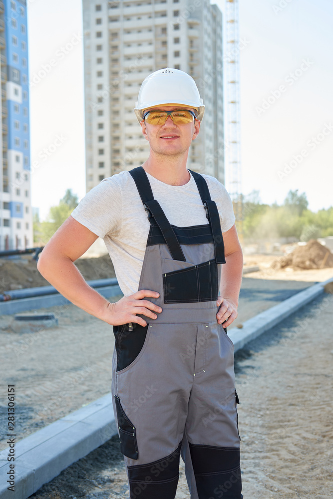Portrait of young handsome hard worker wearing white protective helmet and working overalls at concstruction site Portrait of young handsome hard worker wearing white protective helmet and working overalls at concstruction site
