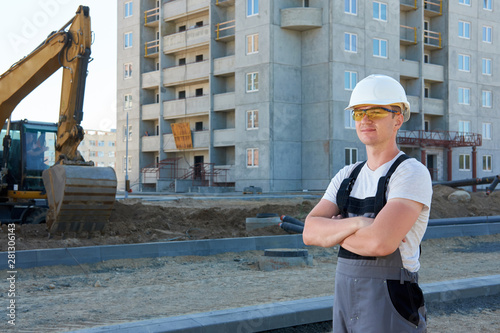 Portrait of young handsome hard worker wearing white protective helmet and working overalls at concstruction site photo