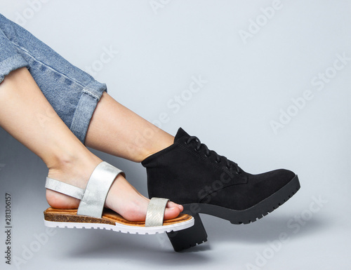 Female legs in jeans shod in boot and sandal sitting on a white background. Creative fashion shot