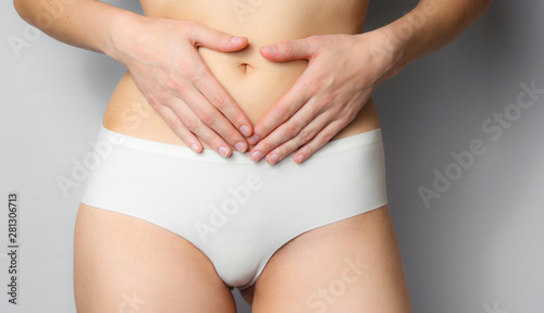 Beauty studio shot. Slim woman in white panties holding her belly on a gray background