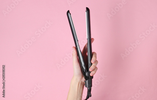 Hair care. Female hand holding hair straightener on pink background. Top view photo