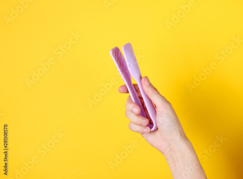 Female hand holding kitchen tweezers on yellow background. Top view