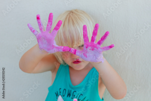 Cute blond toddler girl showing painted pink and violet hands. Focus on hands