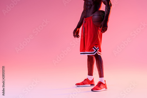 cropped view of shirtless african american basketball player holding ball on pink background with gradient and lighting