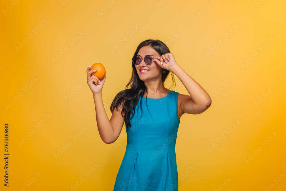 Girl on a yellow background in sunglasses holds orange Girl on a yellow background in sunglasses holds orange