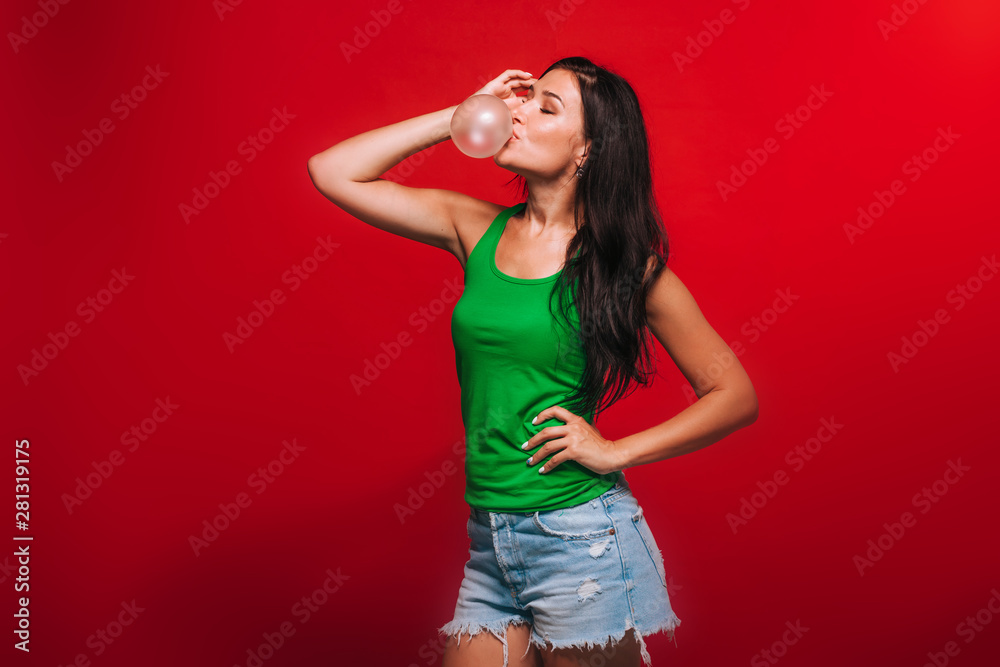 Girl on a red background blowing bubbles of gum