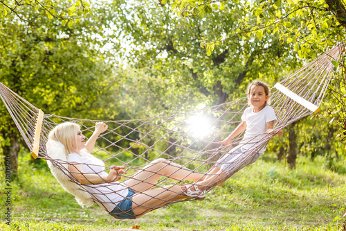 Happy mother and daughter relaxing together in a hammock at garden in sunny summer day. Family playing in hammock.