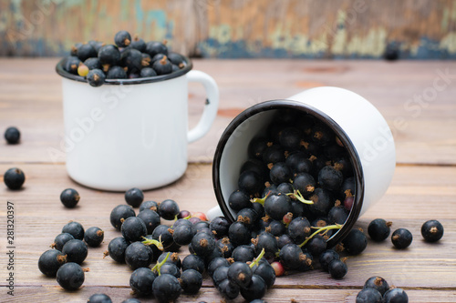 Ripe black currant crumbled out of a white mug on a wooden table