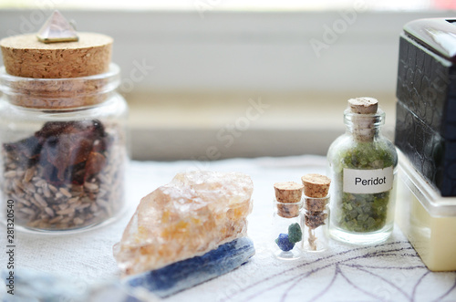 Mystical Peridot in a vial, healing crystals set up on a white cloth. Azurite berries in miniature vial. Crystal display, bohemian decorations on a brightly lit background. Fresh and colorful crystals