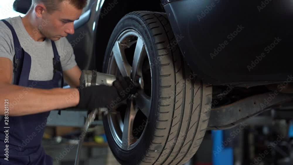 Car mechanic unscrewing car wheel of lifted automobile by pneumatic wrench Car mechanic unscrewing car wheel of lifted automobile by pneumatic wrench