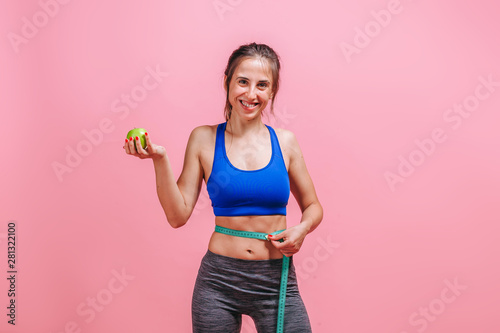 girl measures waist and shows green Apple on pink background © Smeilov
