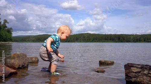 Child (little boy) is standing in a forest lake and playing with stones that he picks up from the bottom of the lake