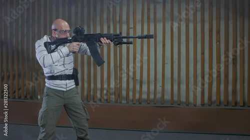 A man trains in target shooting in an indoor shooting range using a high-caliber semi-automatic carbine. 