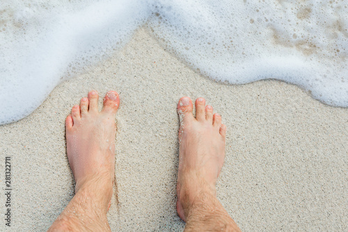 men's feet on sand near sea surf