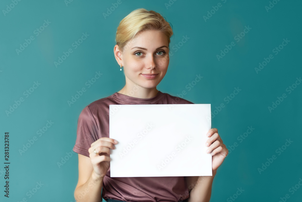 The beautiful girl the blonde smiles and holds in hands a banner, a sheet of paper, with a place for the text. The beautiful girl the blonde smiles and holds in hands a banner, a sheet of paper, with a place for the text.