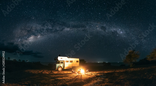 panorama shot of a family sitting at a bonfire under the milky way with a camping truck photo