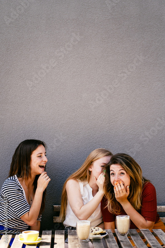 Woman whispering secret at companions ear, gossip together. Female friends sharing time together laughing telling news