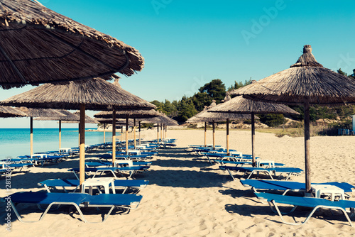 Three rows with straw umbrellas on a beautiful beach in Greece and no people Selective focus