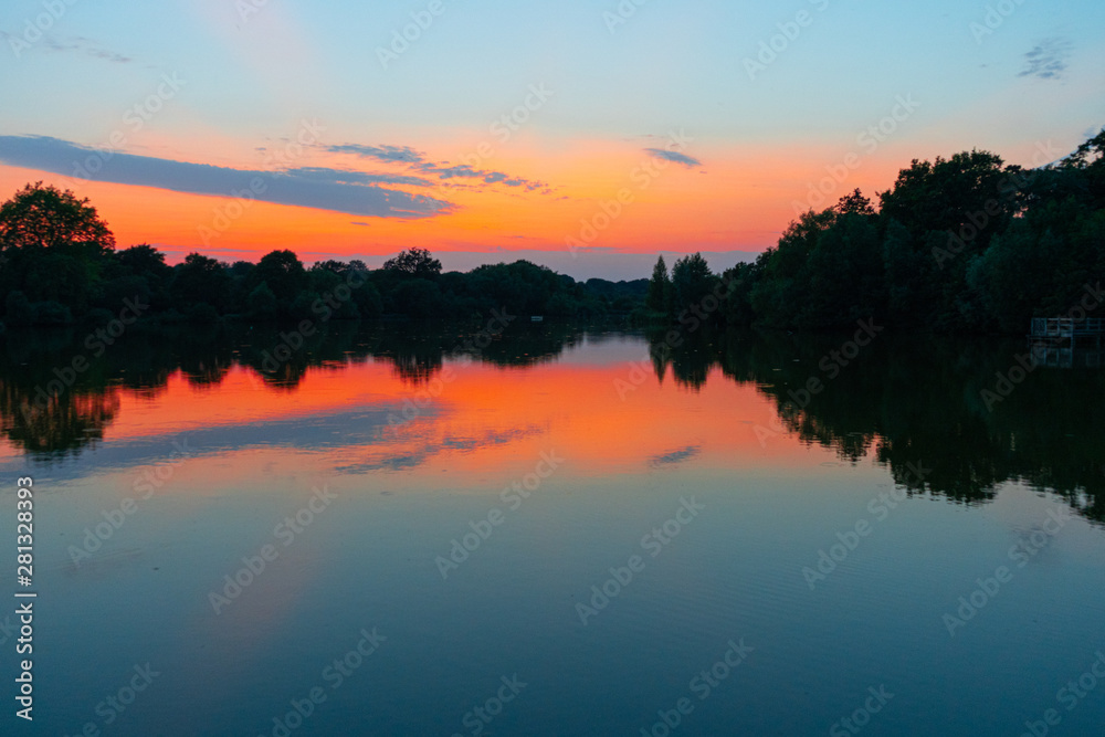 tranquil, twilight sunset shot over lake with reflections of sky and clouds in water and rowing boats to centre of lake