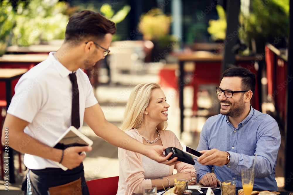 Happy couple paying contactless with smart phone in a bar. Happy couple paying contactless with smart phone in a bar.