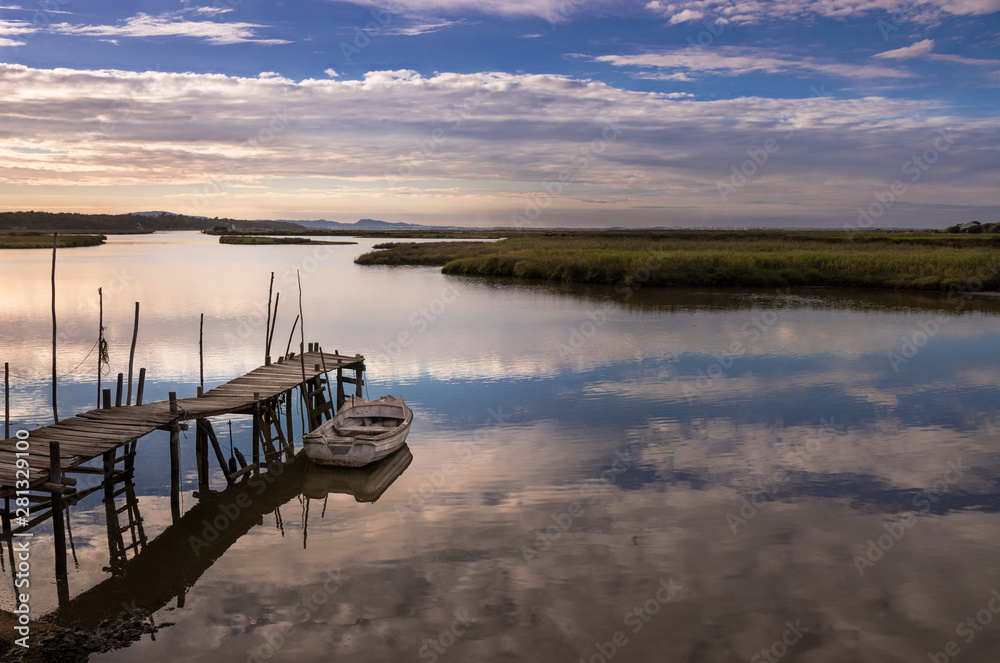 Los palafitos del pueblo de Comporta, en Portugal, durante la puesta de sol, con una barca y las nubes reflejadas en el mar