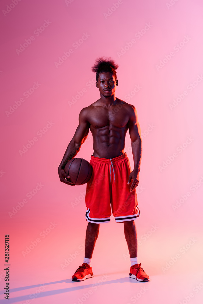 shirtless african american basketball player looking at camera on pink and purple gradient background with lighting