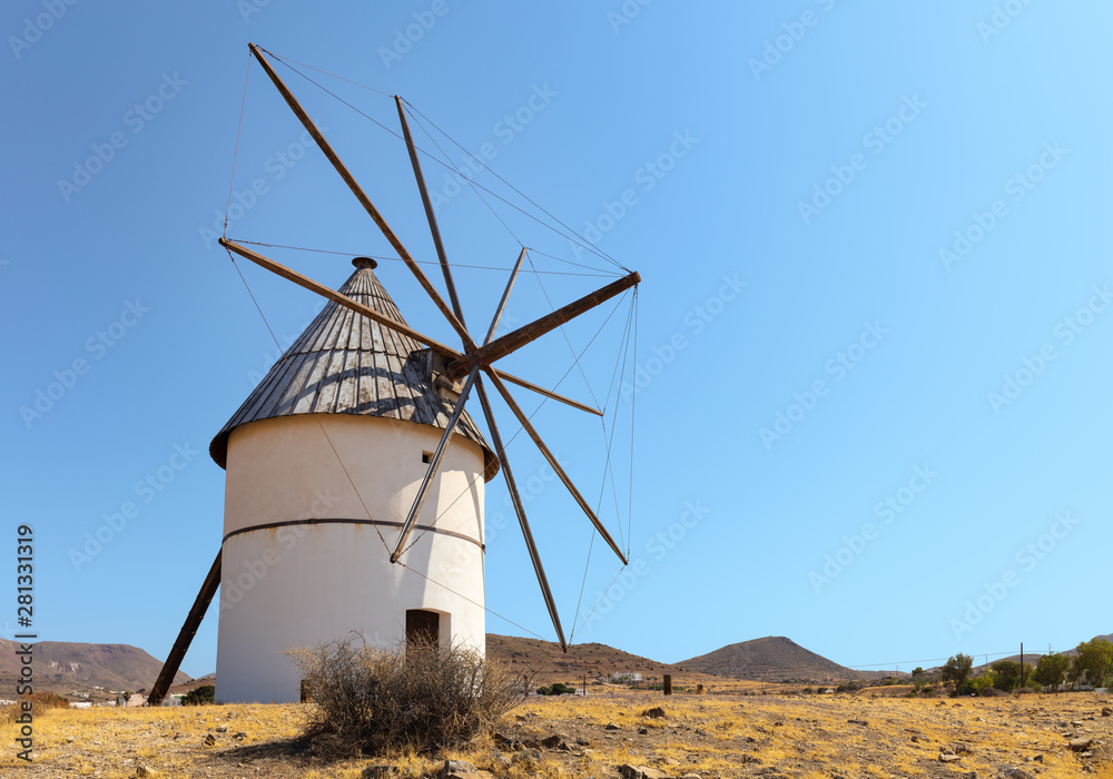 A historic windmill in southern Spain in the village of Pozodelos Frailes near Almeria. The sun shines on the white mill with blue sky.