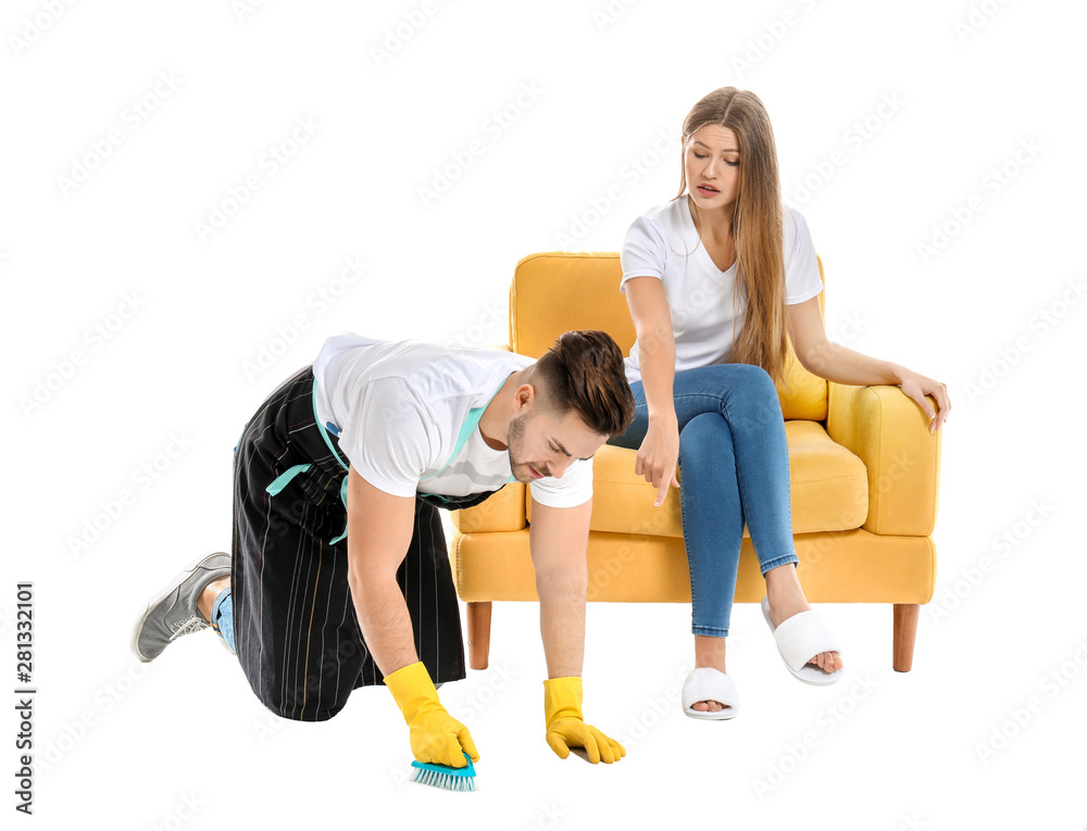 Young husband doing chores while his lazy wife sitting in armchair against white background Young husband doing chores while his lazy wife sitting in armchair against white background