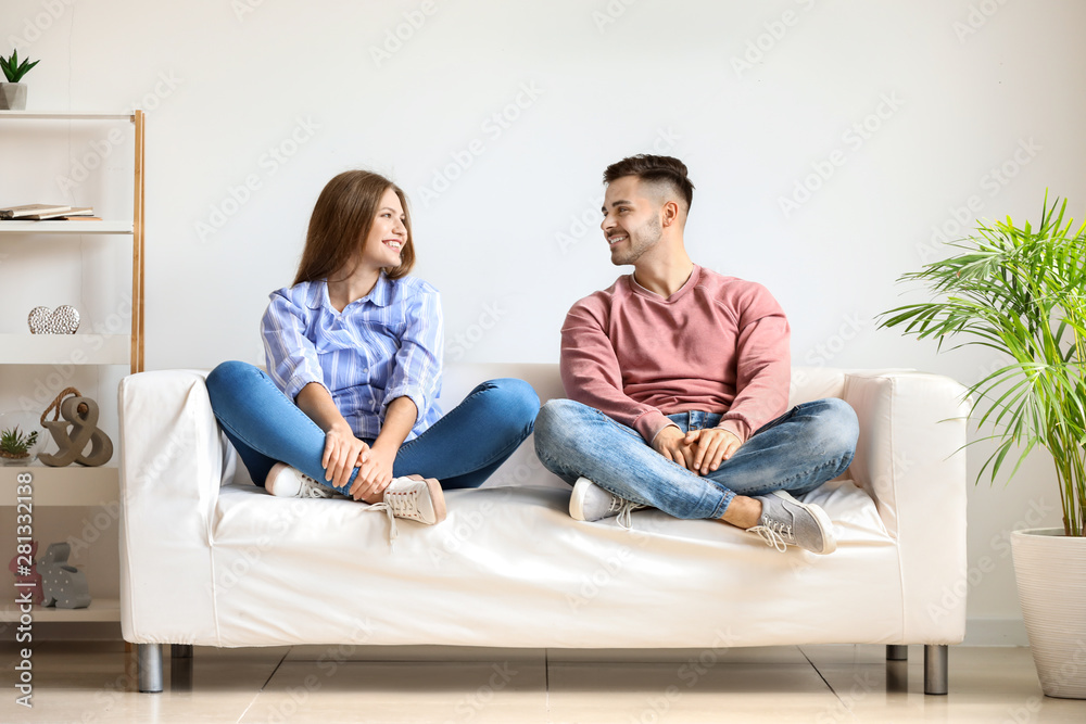 Happy young couple resting together on sofa at home - obrazy, fototapety, plakaty 