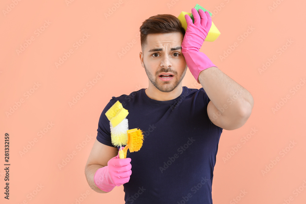 Stressed young man with cleaning supplies on color background Stressed young man with cleaning supplies on color background