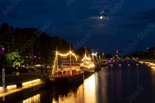 Night view of illuminated restaurant ships with reflection in the water of the river Auraioki, the night landscape of Turku with illumination, the life of the night city. City of Turku, Finland.