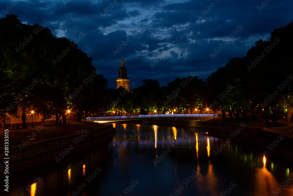 Night view of the historic bridge over the Auraioki River with a reflection in the water against the backdrop of a summer, dark, night cityscape. Turku city, Finnish landmark.
