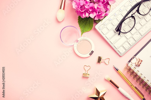 Female workspace with laptop, pink hydrangea, golden accessories, pink diary on pink background.