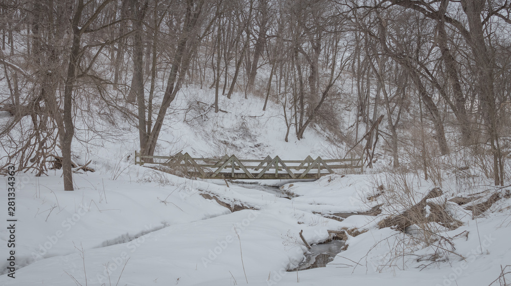 A wooden bridge spans a small creek in a snow covered forest. A wooden bridge spans a small creek in a snow covered forest.